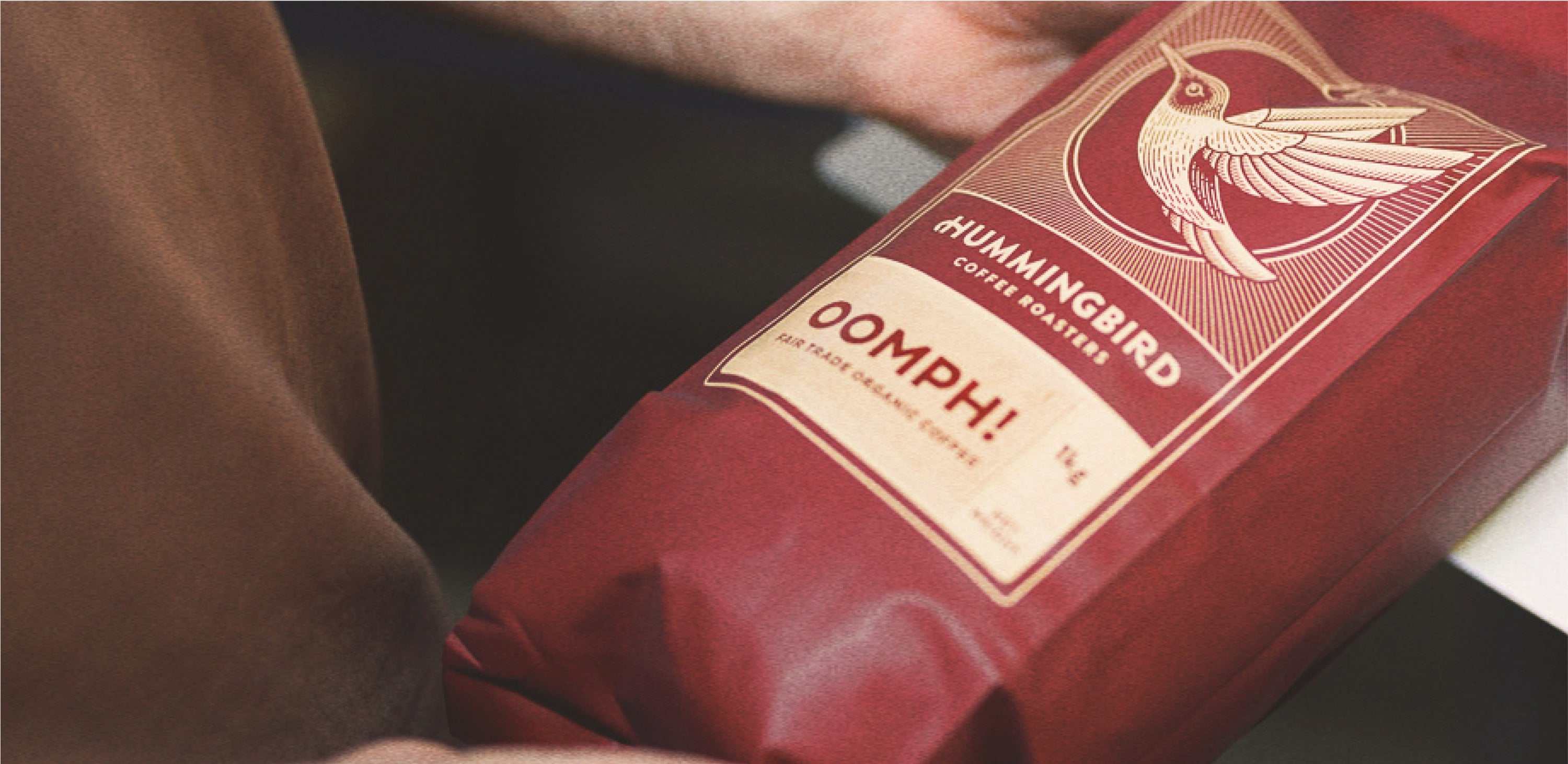A photo of hands holding a red bag of Oomph Hummingbird Coffee
