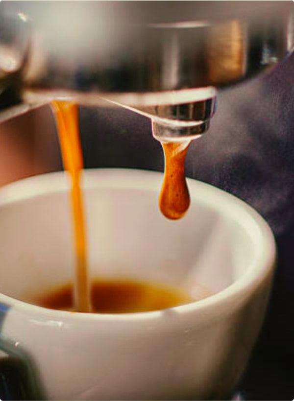 A photo of a drip of golden coffee falling from an Espresso machine into a mug